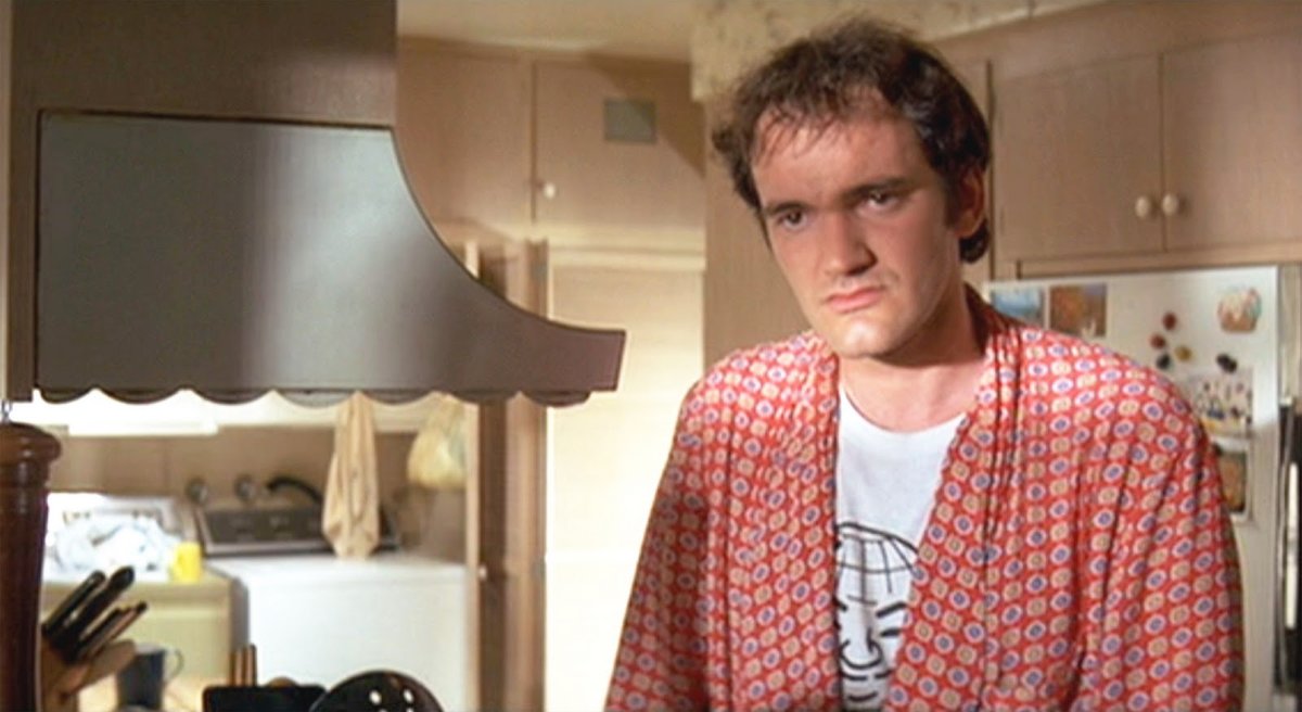 Un uomo in una cucina indossa una vestaglia a motivi geometrici, l'ambiente ricorda una scena familiare in un film.